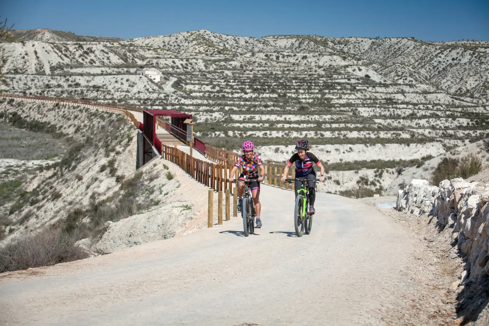 Pasarela metálica roja de la Vía Verde del Chicharra cruzando un paisaje de badlands de yeso blanco al norte de Cieza, sobre el trazado del antiguo ferrocarril de vía estrecha