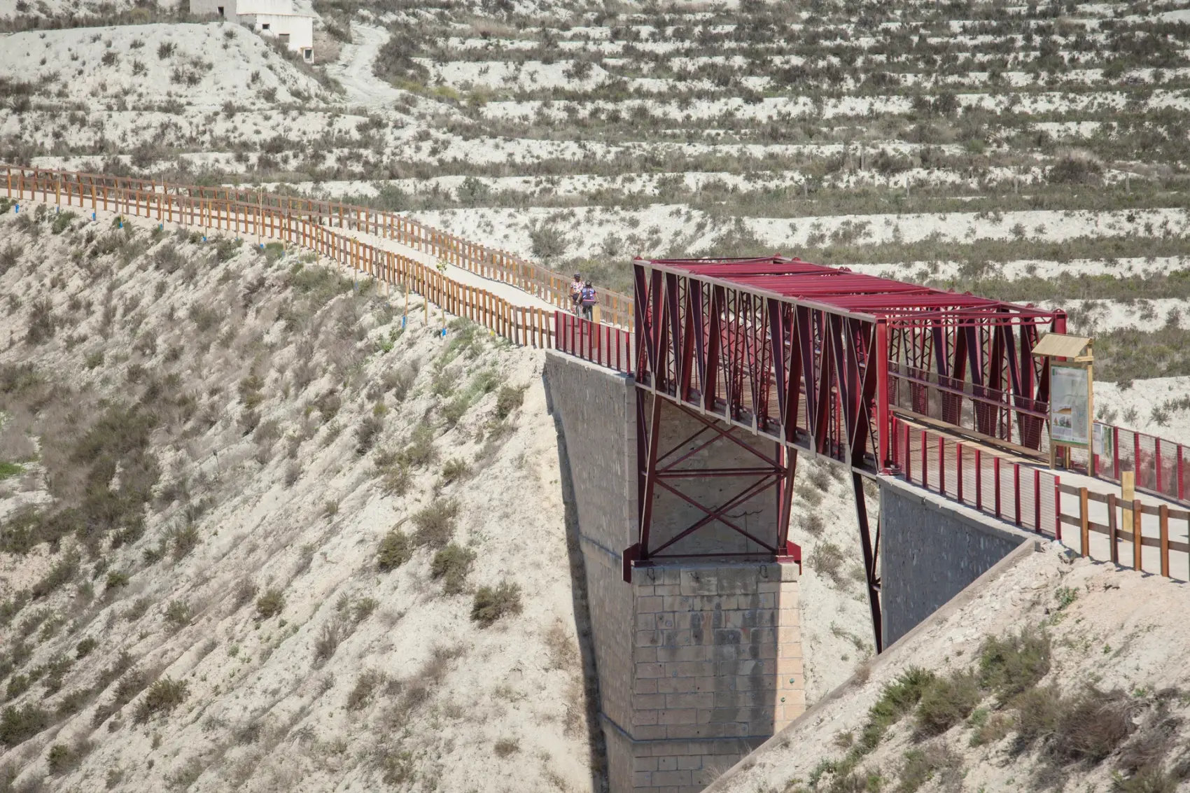 Pasarela metálica roja de la Vía Verde del Chicharra cruzando un paisaje de badlands de yeso blanco al norte de Cieza, sobre el trazado del antiguo ferrocarril de vía estrecha