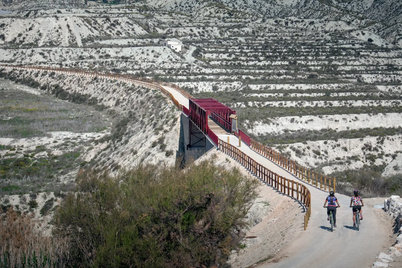 Pasarela metálica roja de la Vía Verde del Chicharra cruzando un paisaje de badlands de yeso blanco al norte de Cieza, sobre el trazado del antiguo ferrocarril de vía estrecha
