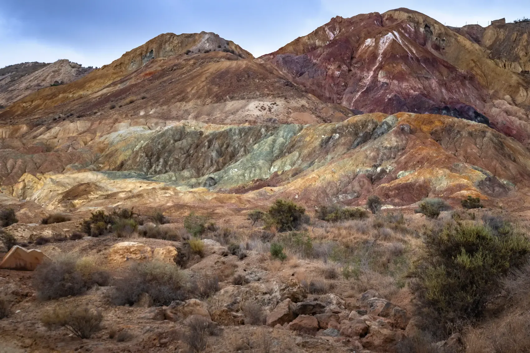 Camino de tierra compactada de la Vía Verde de Mazarrón descendiendo entre los cabezos ocres y rojizos del antiguo Coto Minero de San Cristóbal bajo un cielo azul