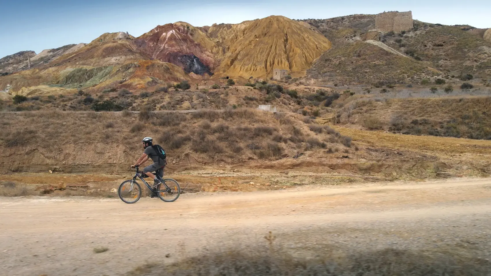 Camino de tierra compactada de la Vía Verde de Mazarrón descendiendo entre los cabezos ocres y rojizos del antiguo Coto Minero de San Cristóbal bajo un cielo azul