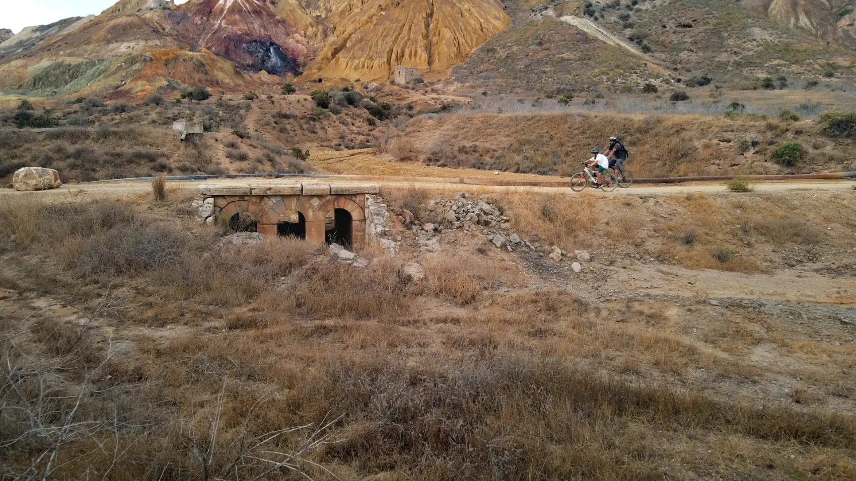 Camino de tierra compactada de la Vía Verde de Mazarrón descendiendo entre los cabezos ocres y rojizos del antiguo Coto Minero de San Cristóbal bajo un cielo azul