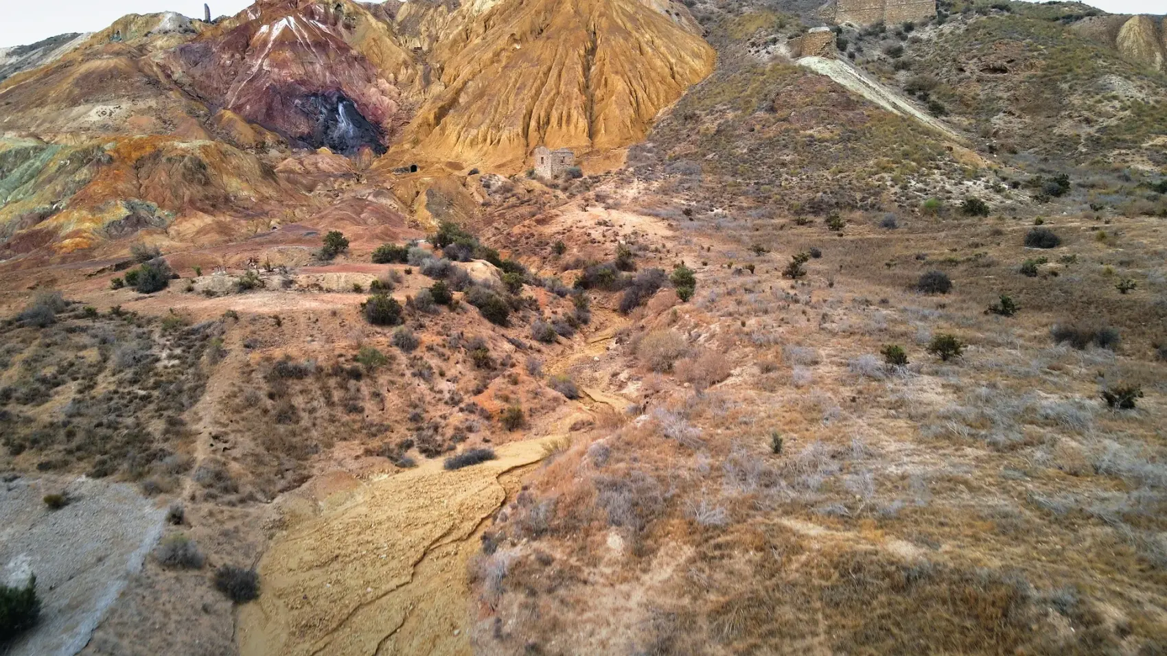 Camino de tierra compactada de la Vía Verde de Mazarrón descendiendo entre los cabezos ocres y rojizos del antiguo Coto Minero de San Cristóbal bajo un cielo azul
