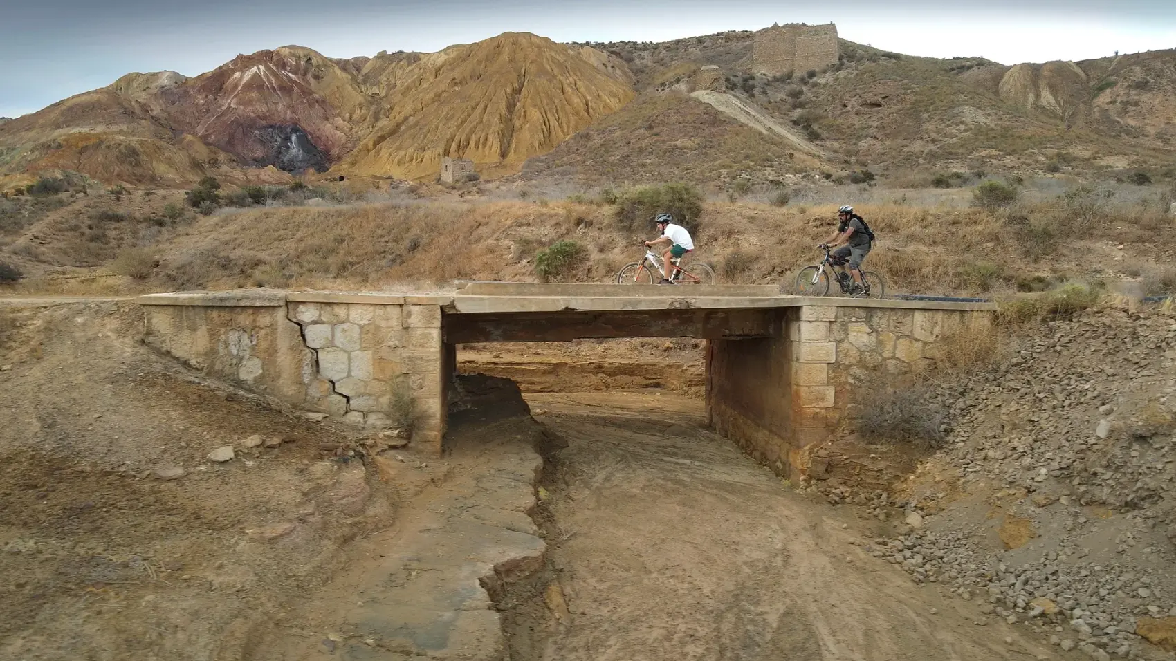 Camino de tierra compactada de la Vía Verde de Mazarrón descendiendo entre los cabezos ocres y rojizos del antiguo Coto Minero de San Cristóbal bajo un cielo azul